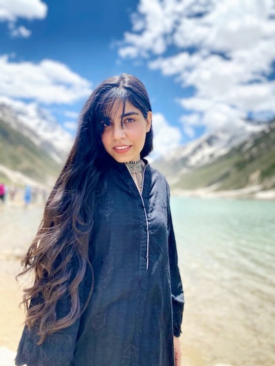 A portrait image of Hijjab Waqar Hussein in front of a lake and mountains in Pakistan