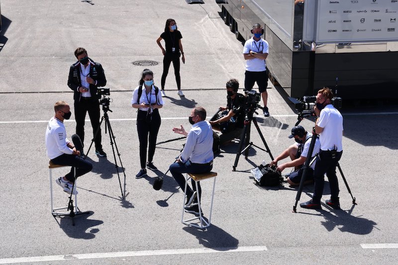 Image shows Georgina Sadler in a group helping film a piece to camera with Martin Brundle, bottom centre, and Valteri Bottas, bottom left